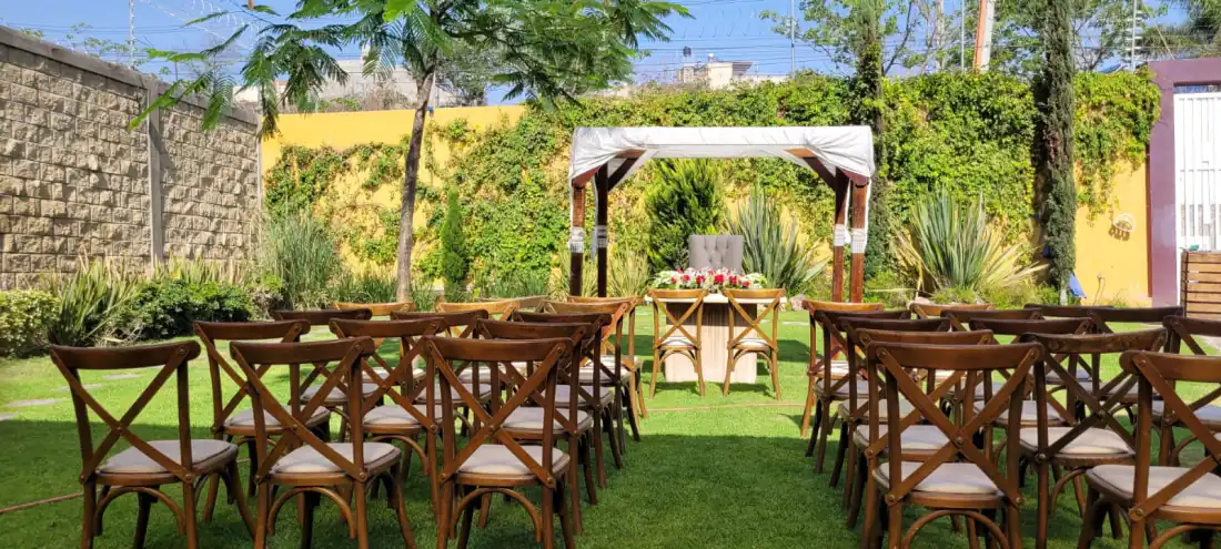 Jardín para bodas en Bonanza: pérgola blanca entre muros de enredadera, con sillas de madera listas para la ceremonia