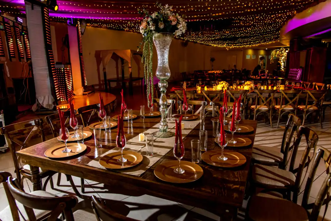 Salón de bodas de noche, con cielo de luces cálidas y mesas montadas con plato base dorado